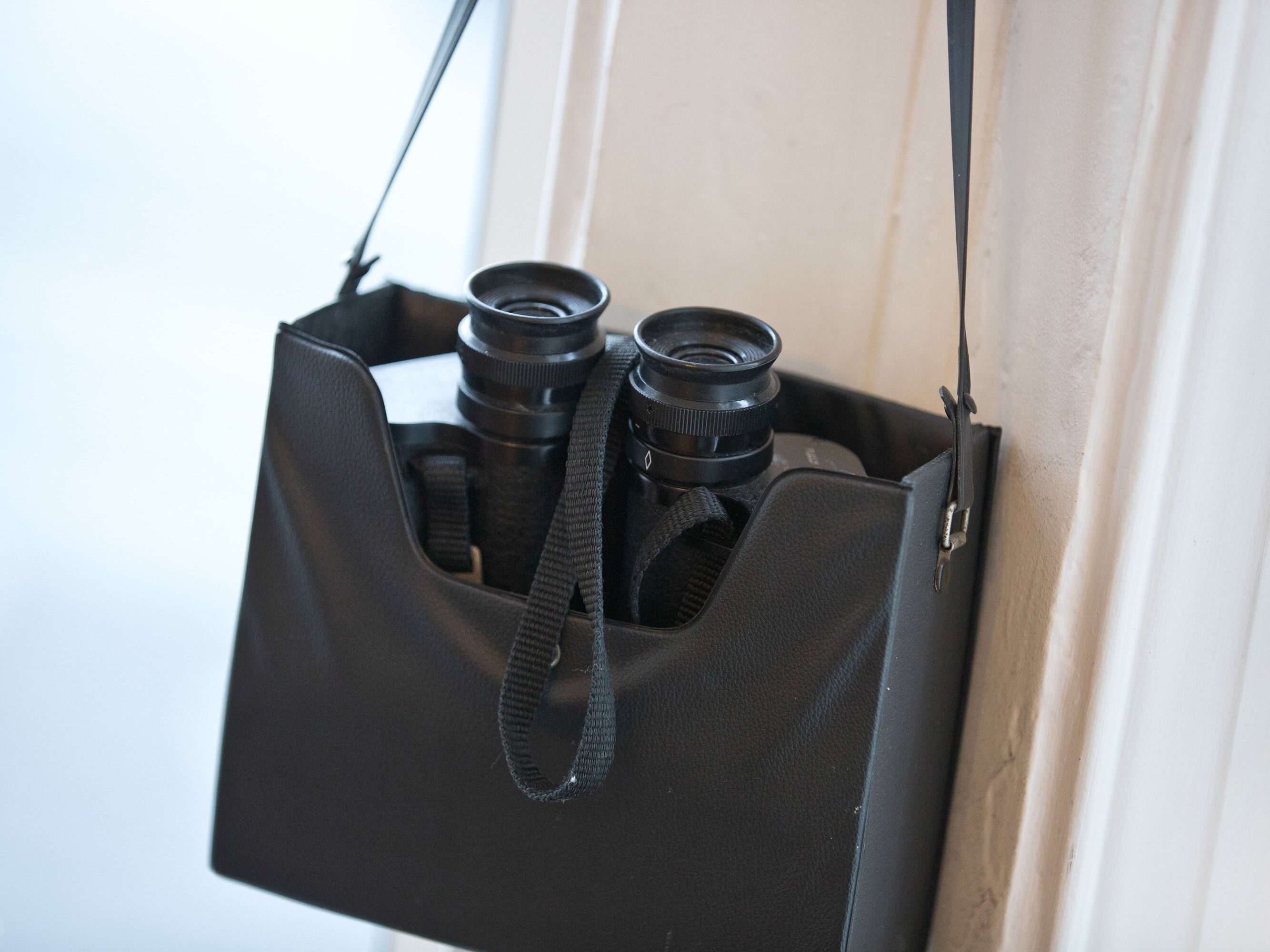 Un sac pour appareil photo noir, contenant deux objectifs et muni d’une bandoulière.