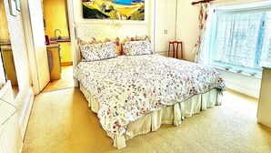 A bedroom with a bed, a painting, a window with curtains, and a door leading to a bathroom. - Seafront Apartments (North Shields)