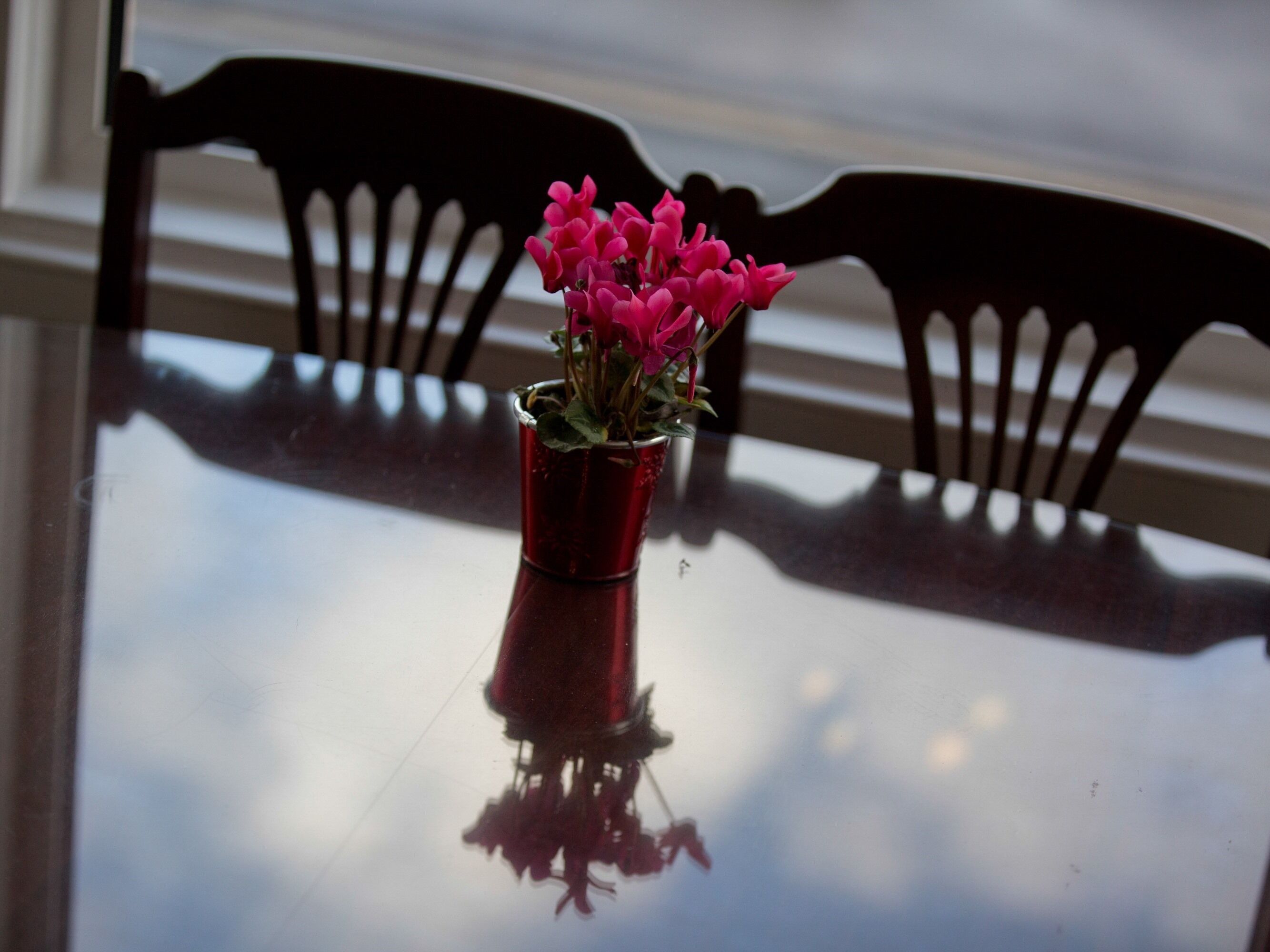 A table with a red vase containing pink flowers, reflecting on its surface.