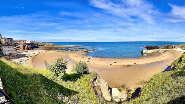 A coastal beach with a sandy shore, a small pier, and buildings in the background. - Seafront Apartments (North Shields)