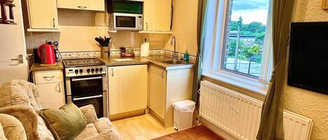 A compact kitchen with basic appliances, a dining area with a table and chairs, and a window with a view of greenery outside.