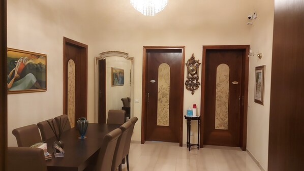 Un comedor con una mesa y sillas, una araña y una puerta con espejo y reloj.