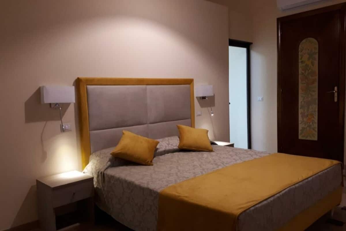 Un dormitorio con una cama, dos lámparas de noche, una mesita de noche, una puerta con diseño floral y un equipo de aire acondicionado.