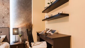 A bedroom with a bed, a desk, and a chair. There is a lamp, a vase with flowers, and a shelf with decorative items. - Beautiful Safe Apartment Near Centre (Athens)