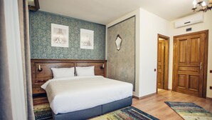 A bedroom with a large bed, wooden headboard, two framed pictures on the wall, a mirror, and a wooden door. - Pensiunea Kant (Sibiu)