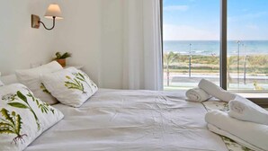 Ett hotellrum med en säng, kuddar, en lampa och utsikt över havet.