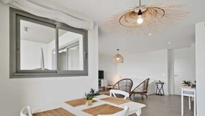 Ett modernt matområde med ett stort fönster, vita möbler och en vävd taklampa.
