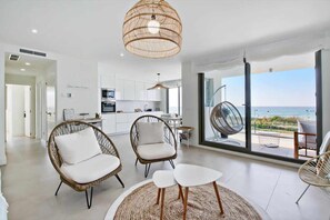 Uma sala de estar moderna com cadeiras de vime, uma mesa de centro branca e vista para o oceano.