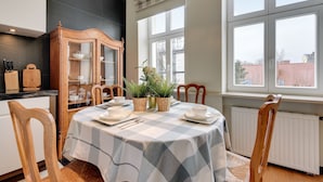Un comedor con mantel a cuadros, sillas de madera, un aparador con puertas de cristal y plantas en macetas.