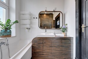 Une salle de bain moderne avec une baignoire blanche, un meuble-lavabo en bois, un grand miroir et un radiateur.