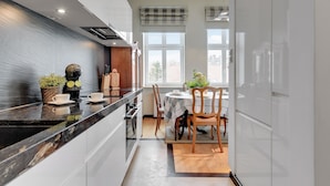 Una cocina moderna con encimera de mármol negro, armarios blancos y un comedor con mesa y sillas.