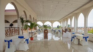 A spacious indoor area with white tables and chairs, some with blue sashes, and a tiled floor. - Hotel Hibiscus Louis (Libreville)