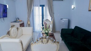 A living room with a white sofa, a green sofa, a coffee table, a TV, and a window with curtains. - Hotel Hibiscus Louis (Libreville)