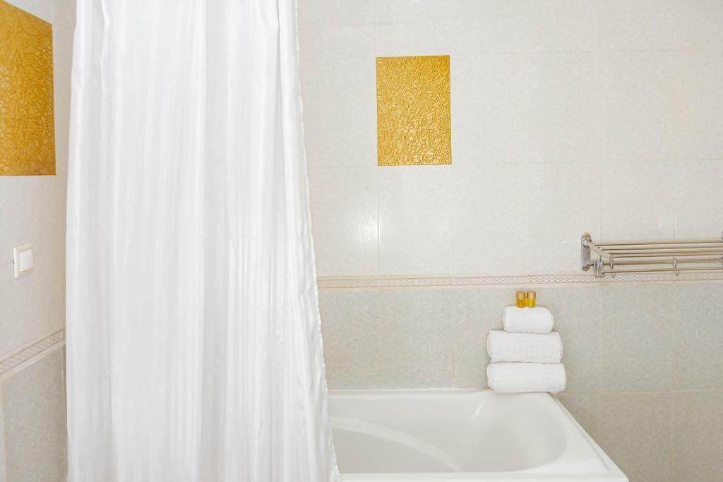 Une salle de bain avec une baignoire, un porte-serviettes avec des serviettes pliées et un mur d’accent doré.