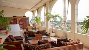 A spacious lounge area with multiple seating options, including sofas and chairs, arranged around a central coffee table. Large windows provide a view of the cityscape. - Hotel Hibiscus Louis (Libreville)