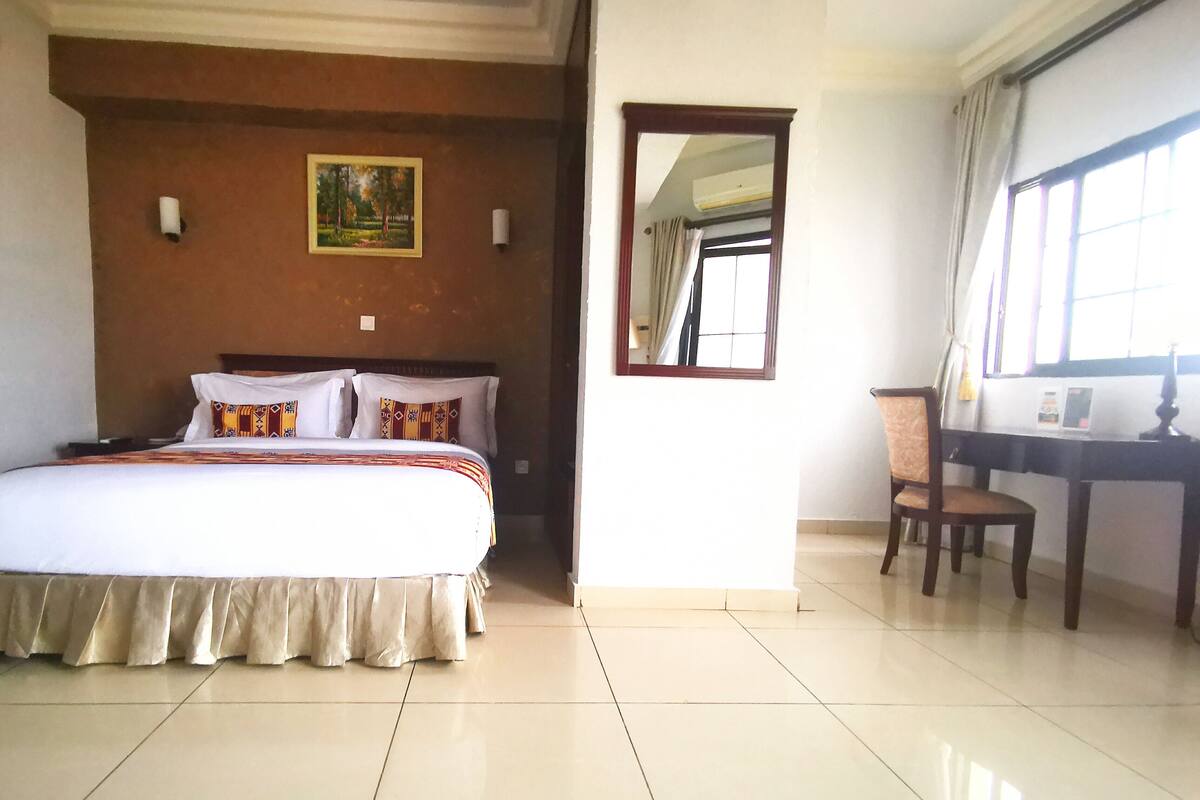 A hotel room with a bed, a desk, a chair, a painting on the wall, and a window.