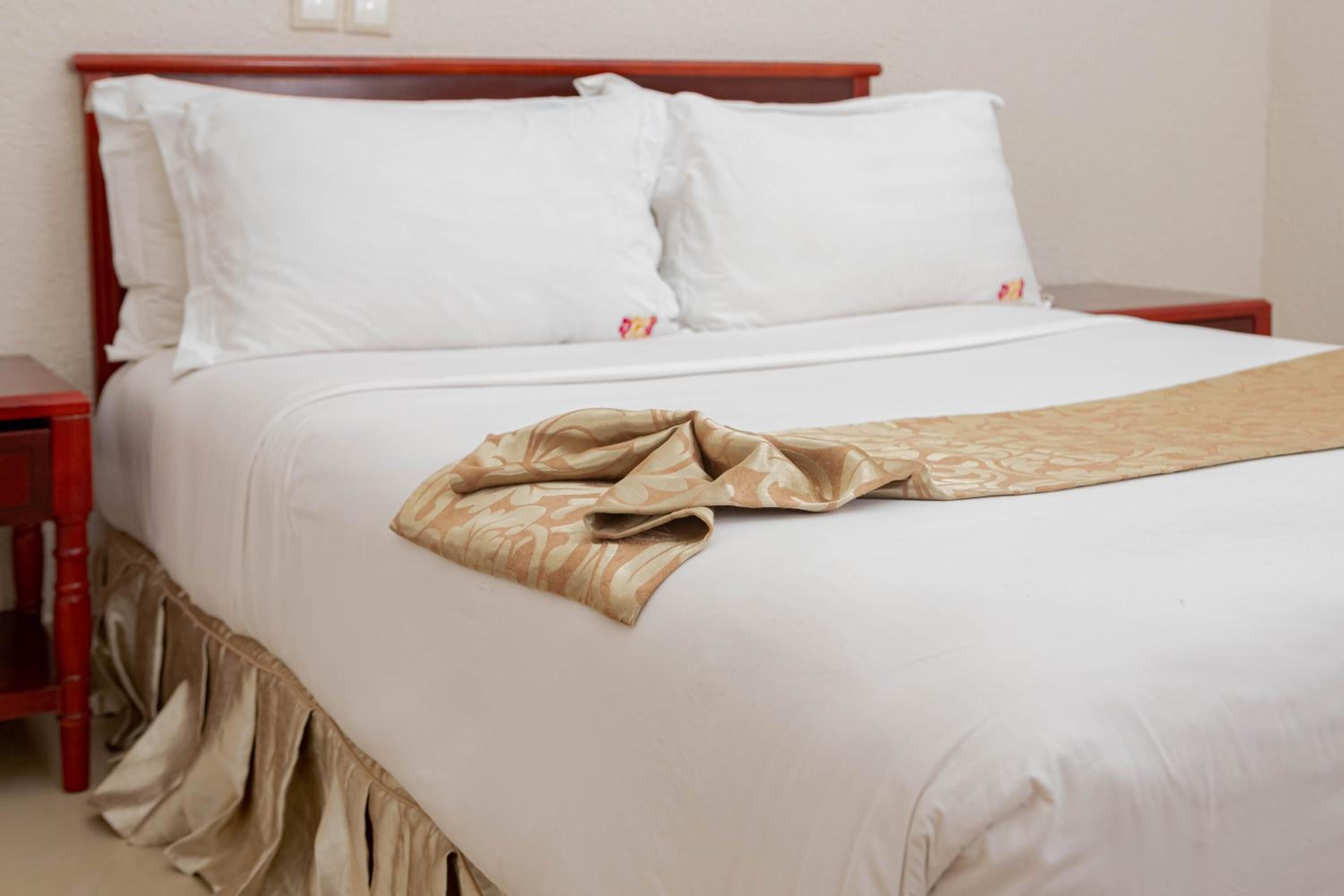 A neatly made bed with white linens and a beige throw blanket.