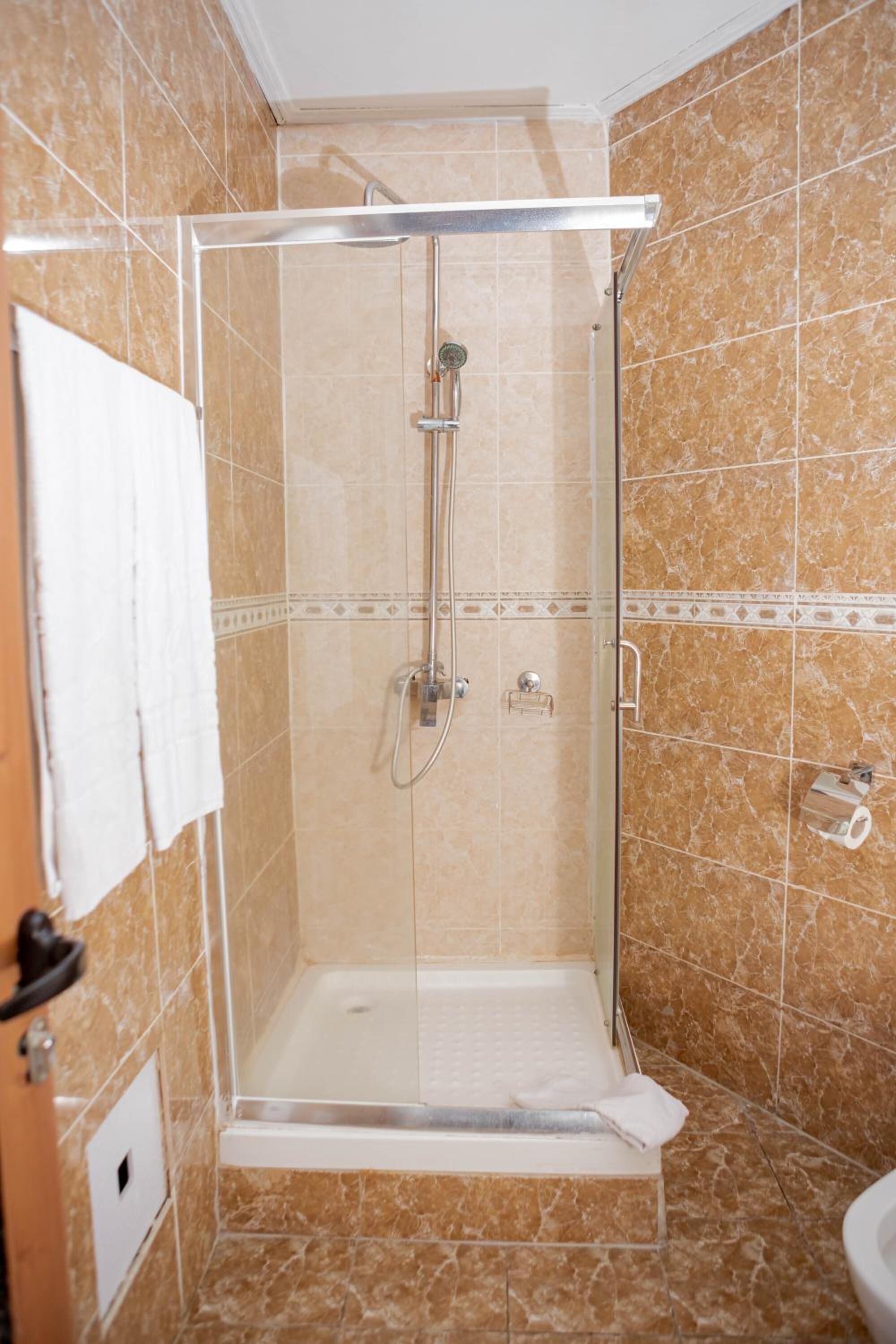 A glass-enclosed shower stall with a white floor, a handheld showerhead, and a wall-mounted faucet.