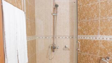 A glass-enclosed shower stall with a white floor, a handheld showerhead, and a wall-mounted faucet.