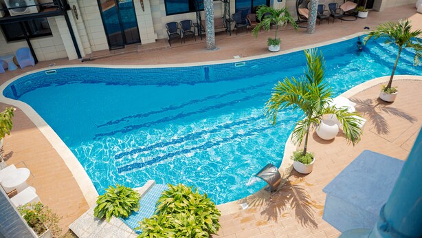 A swimming pool with a tiled deck, surrounded by potted plants and outdoor furniture. - Hotel Hibiscus Louis (Libreville)