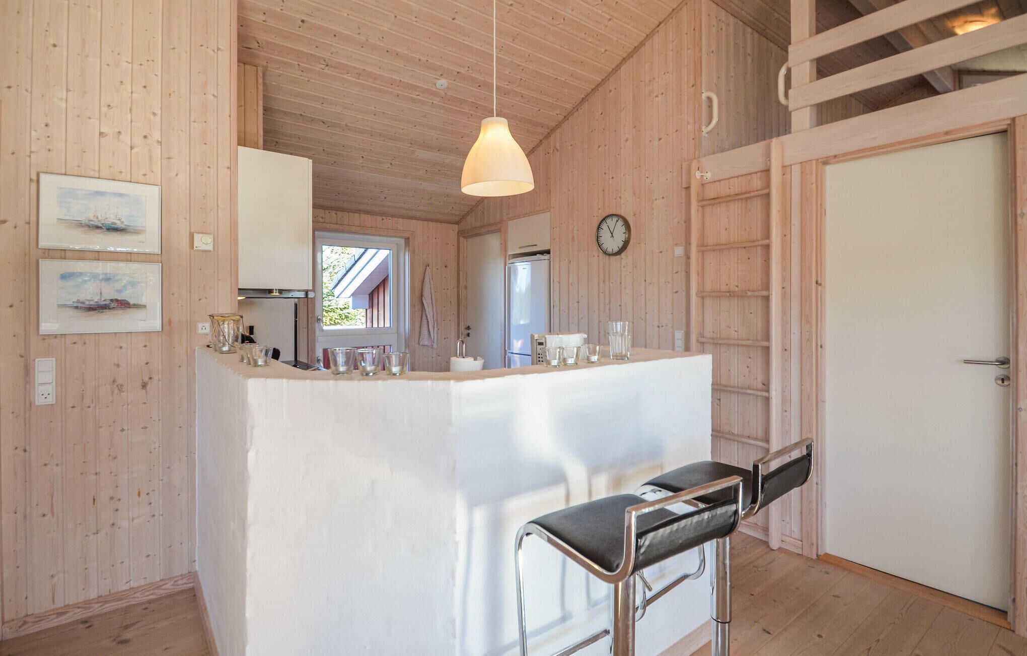 Un interior de fusta amb una barra de cuina, tamboretes, un rellotge i quadres a la paret.