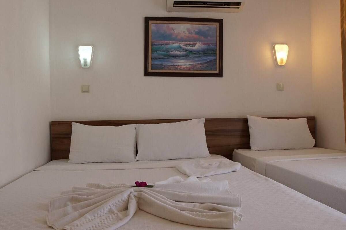 Een hotelkamer met twee bedden, een schilderij van de oceaan en twee wandlampen.