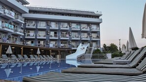 A hotel with a swimming pool, sun loungers, and a covered area with umbrellas.
