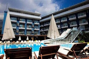 A hotel with a swimming pool, lounge chairs, and umbrellas.