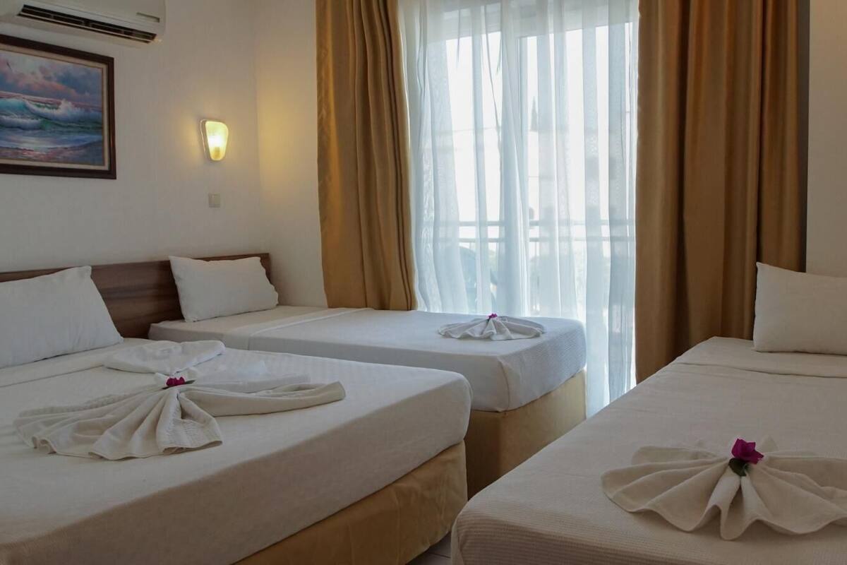 Een hotelkamer met twee bedden, elk voorzien van handdoeken en een roze bloem. Op de muur hangt een schilderij en er is een raam met gordijnen.