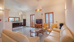 Un salón espacioso con sofá, mesa de centro y televisión. Cuenta con una zona de cocina con nevera y ventana.