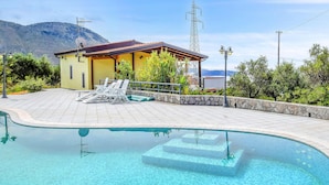Una piscina con agua cristalina azul, rodeada por una terraza empedrada y sillones de descanso.