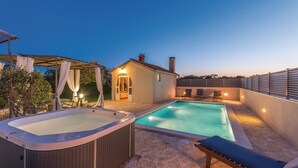 Un espace piscine aménagé sur le toit, comprenant un jacuzzi, des chaises longues et un petit bâtiment doté d’une porte et de fenêtres.