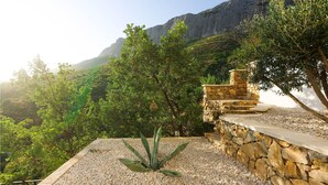 A garden with a stone wall and a view of a mountainous landscape. - Cozy home in Zrnovnica (Zrnovnica)