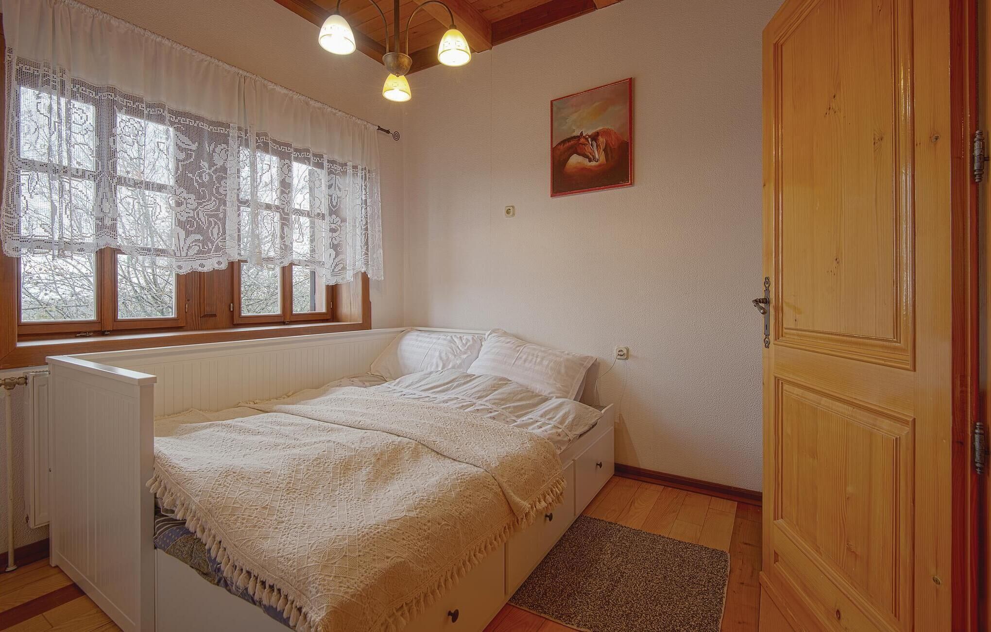 Un dormitorio con cama, un radiador, una ventana con cortinas de encaje, un cuadro y una puerta de madera.