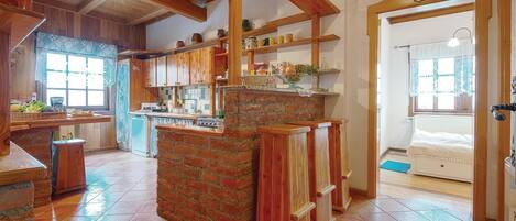 A rustic kitchen with wooden beams, a brick island, and a tiled floor.