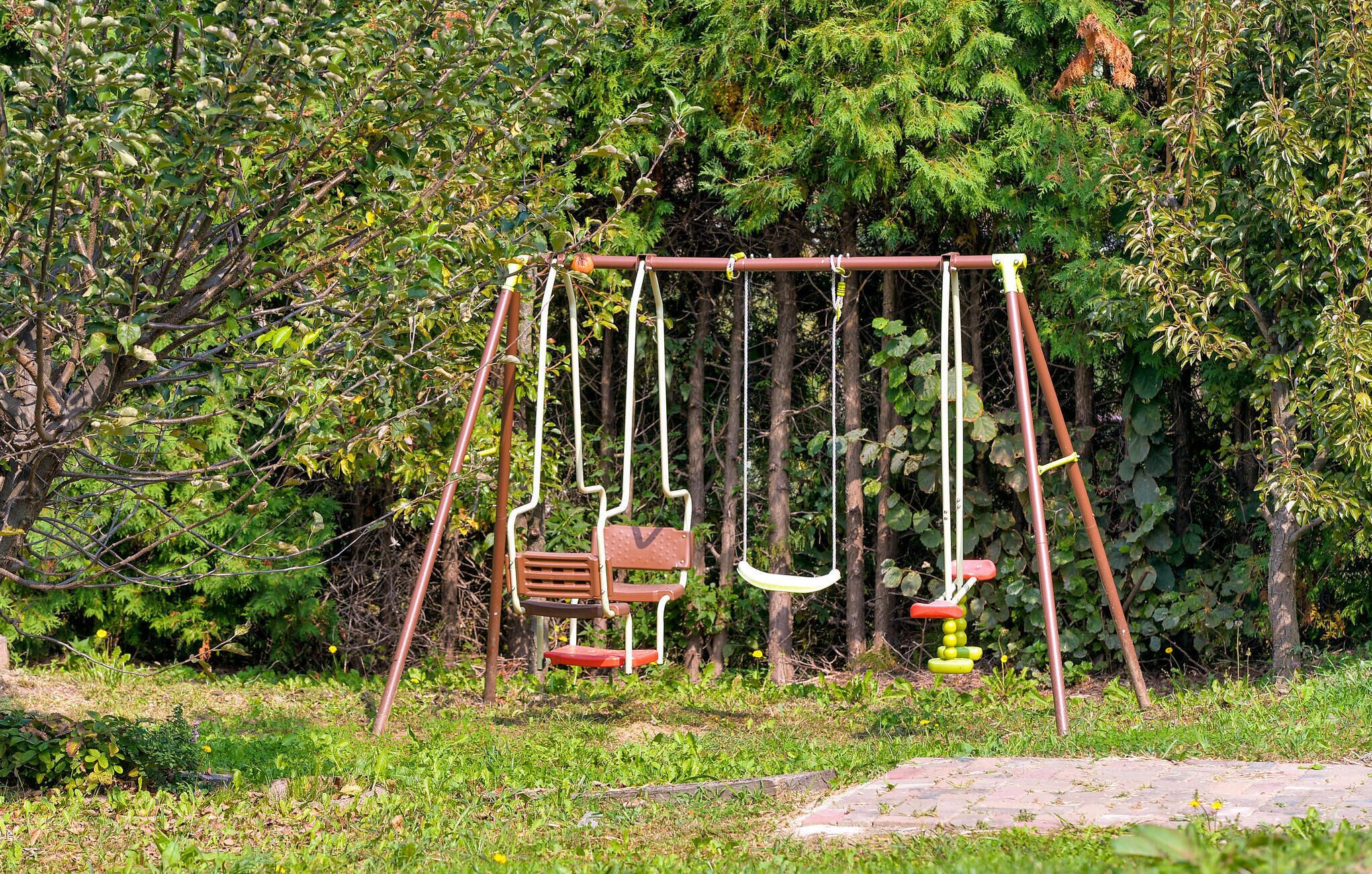 A swing set in a garden with dense foliage in the background.