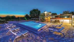 En swimmingpool med liggestole, et legerum for børn og et moderne hus med balkon.