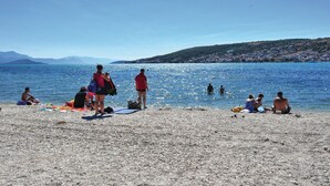 En stenstrand med folk, der solbader og svømmer.