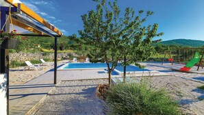 Et poolområde med et pergola, liggestole, et lille træ og en børnerutsjebane.