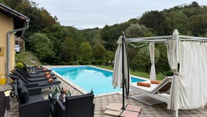 A poolside area with lounge chairs and a canopy, surrounded by lush greenery.