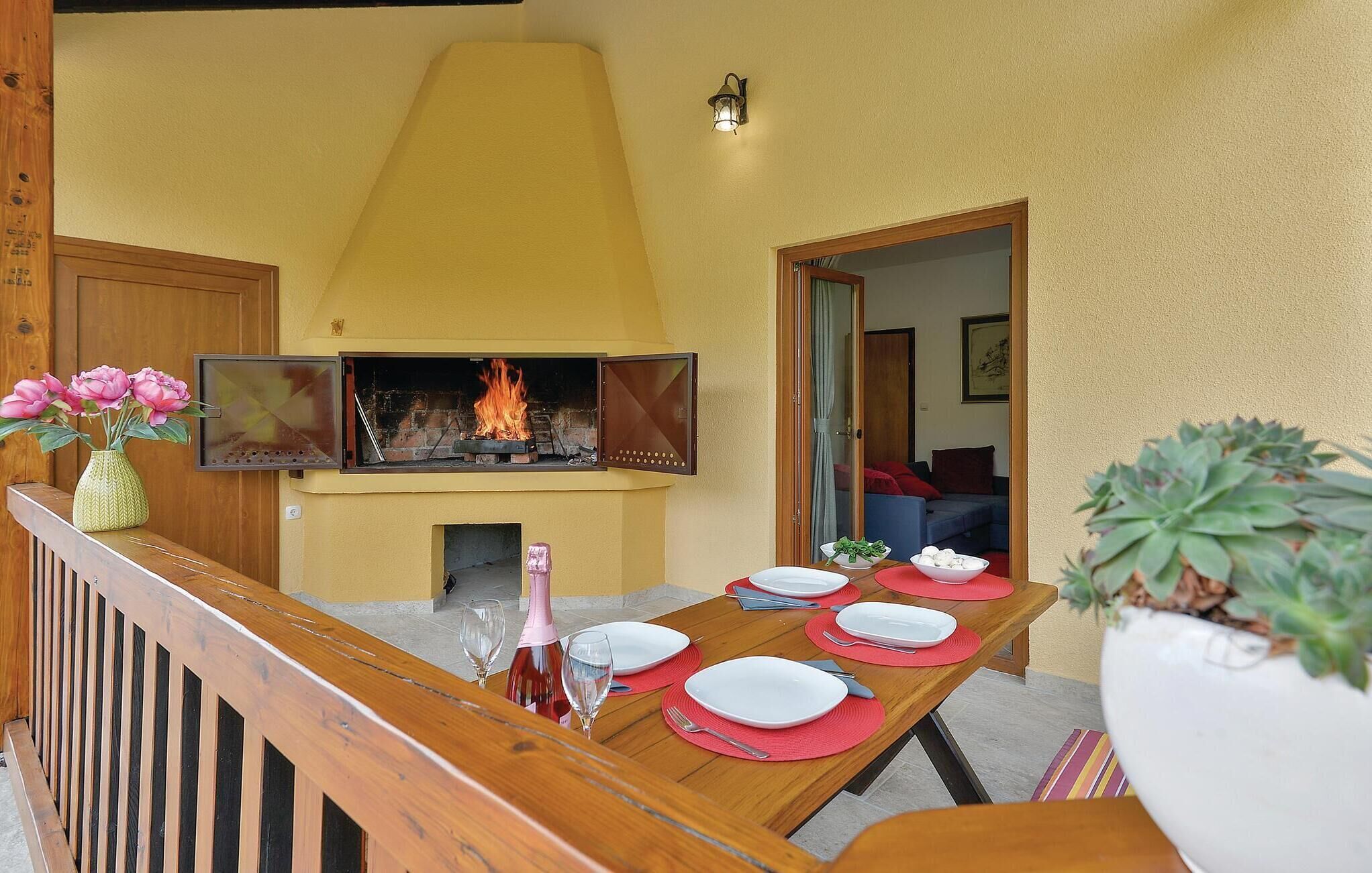Un coin repas avec une cheminée, une table en bois dressée pour quatre personnes et une plante en pot sur la droite.
