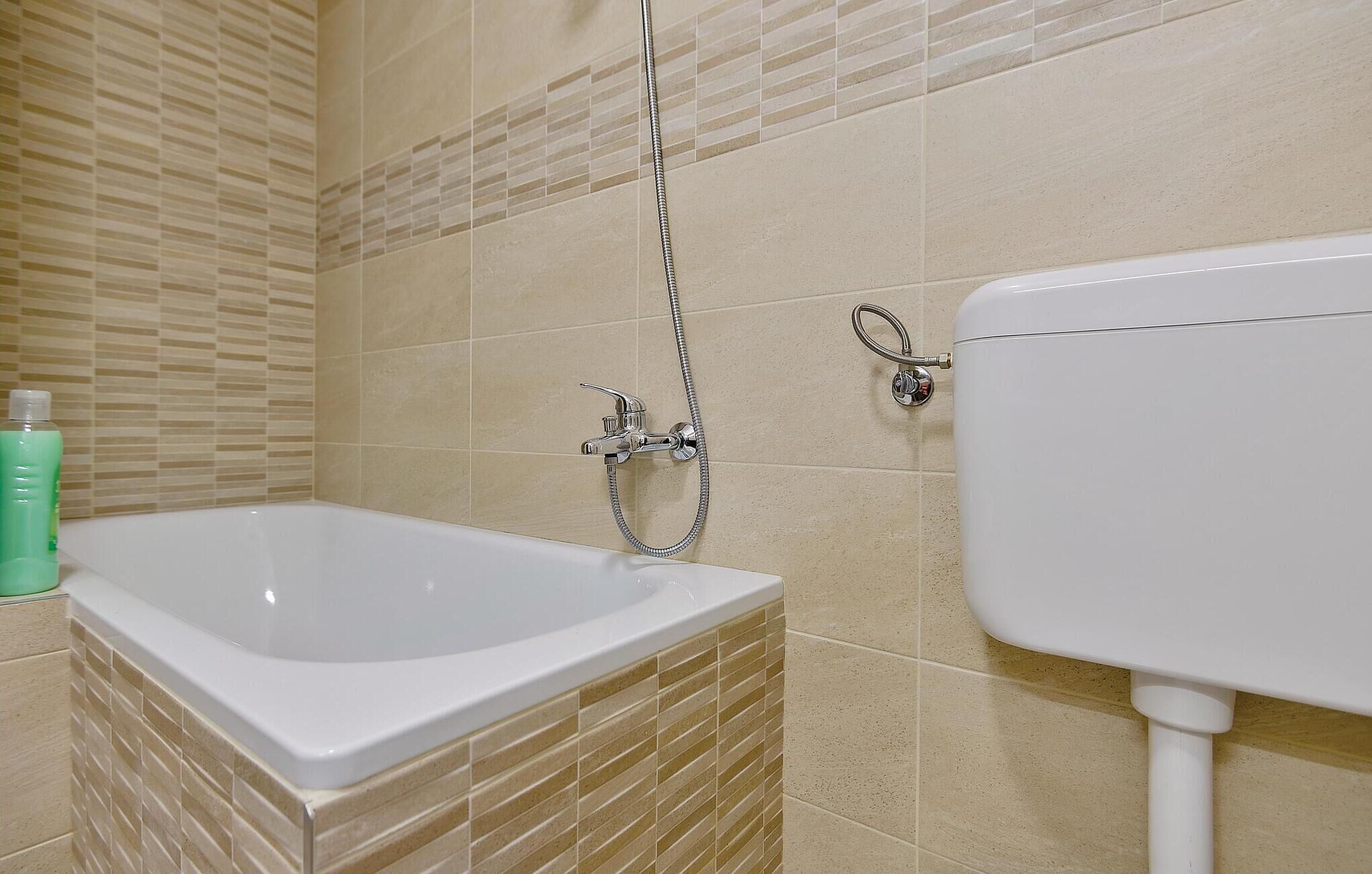 Un baño con una bañera blanca, cabezal de ducha y un inodoro.