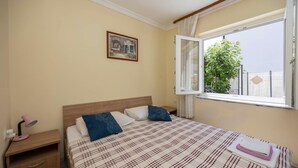 A bedroom with a bed, a nightstand, a window with a view of greenery, and a painting on the wall. - 2 bedroom gorgeous apartment in Okrug Gornji (Okrug Gornji)
