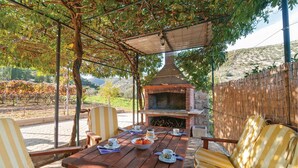 Une terrasse extérieure avec un barbecue en briques, une table en bois, des chaises à rayures et une vue sur un vignoble.