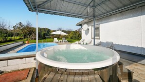 Una vasca idromassaggio sotto un portico coperto, una piscina e sedie a sdraio.