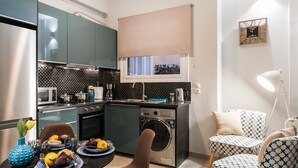 A compact kitchen with modern appliances, a dining area with a table set for two, and a small seating area with patterned chairs. - Central Safe Smart Apartment (Athens)