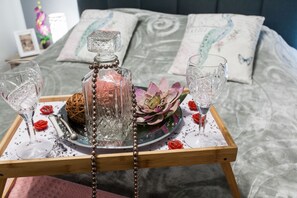 A tray with a perfume bottle, two glasses, and decorative items on a bed.