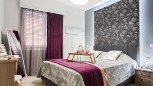 A bedroom with a bed, bedside table, curtains, and a wall with a floral pattern. - Central Safe Smart Apartment (Athens)