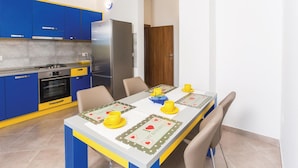 Une cuisine compacte avec des meubles bleus, un réfrigérateur en acier inoxydable, une cuisinière et une table à manger agrémentée de tasses jaunes et d’une carte décorative.