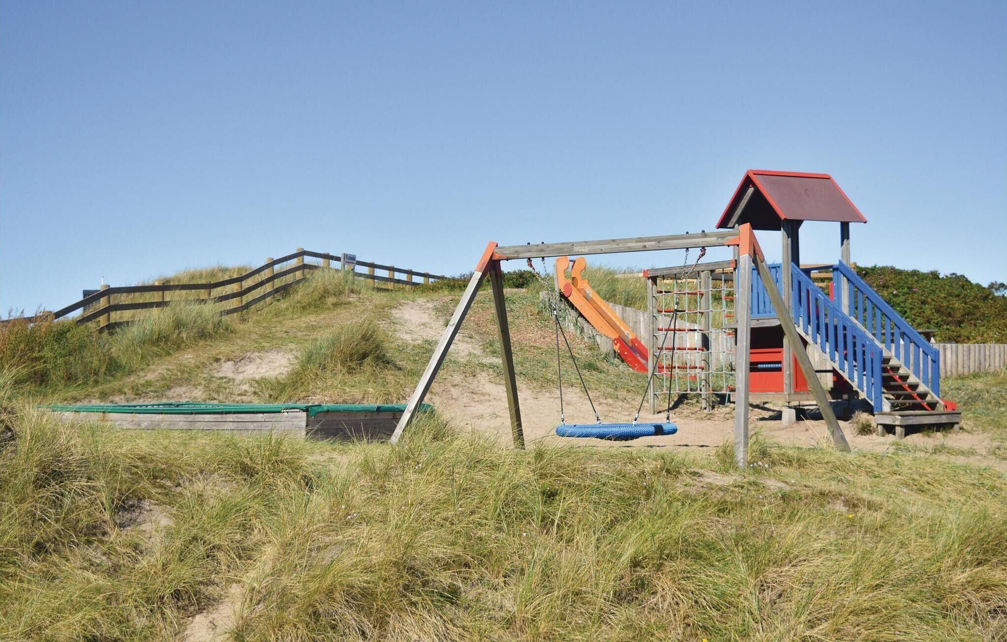 Une aire de jeux avec un toboggan, des balançoires et un petit bâtiment doté d’un escalier.
